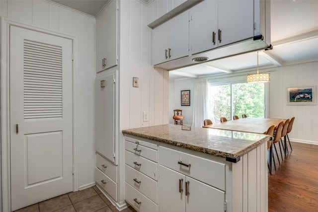 kitchen featuring crown molding, kitchen peninsula, light stone countertops, hanging light fixtures, and hardwood / wood-style floors