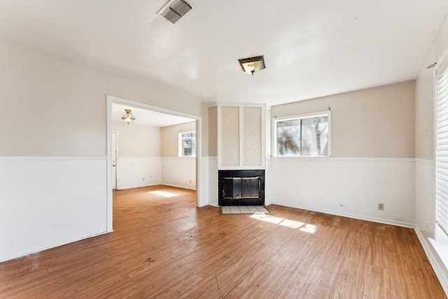 unfurnished living room featuring a multi sided fireplace, visible vents, wainscoting, and wood finished floors