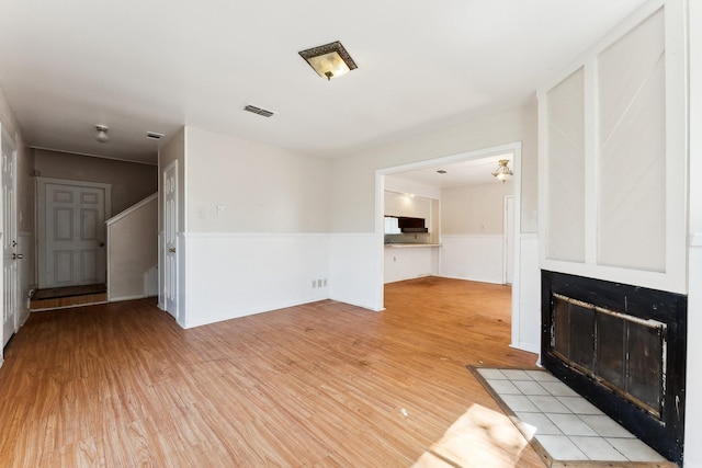 unfurnished living room with light wood-style flooring, a fireplace with flush hearth, and a wainscoted wall