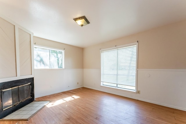 unfurnished living room featuring a tiled fireplace, wood finished floors, and baseboards