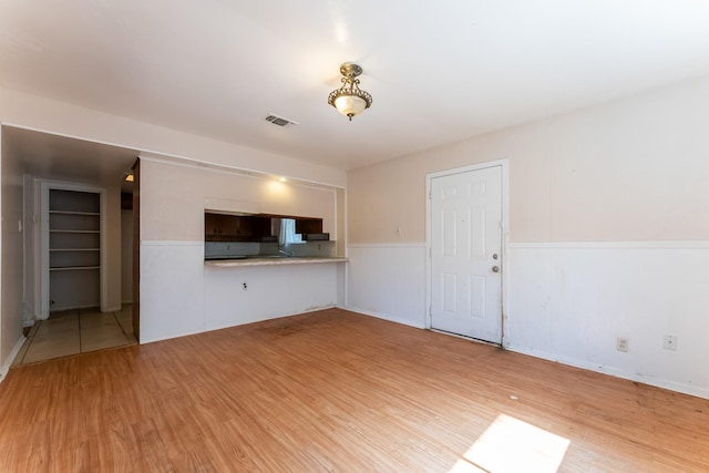 unfurnished living room with a wainscoted wall, light wood-style flooring, and visible vents