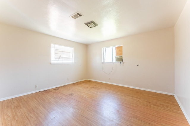 empty room featuring cooling unit, light wood-style floors, visible vents, and baseboards