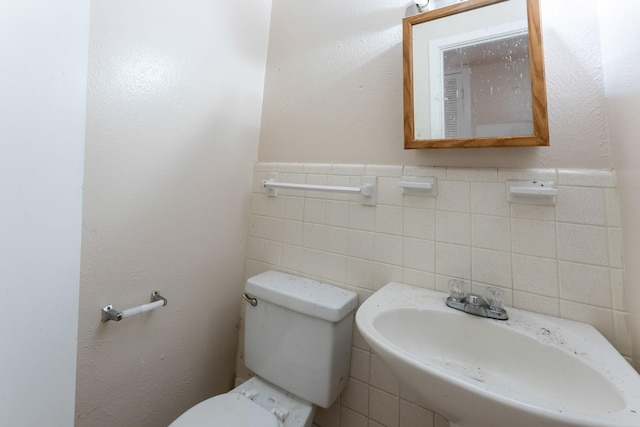 bathroom featuring tile walls, toilet, a wainscoted wall, and a sink