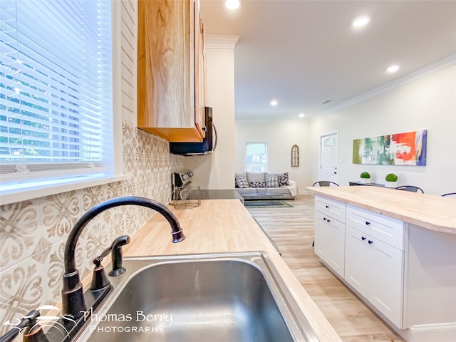 kitchen featuring sink, butcher block counters, light wood-type flooring, white cabinetry, and ornamental molding