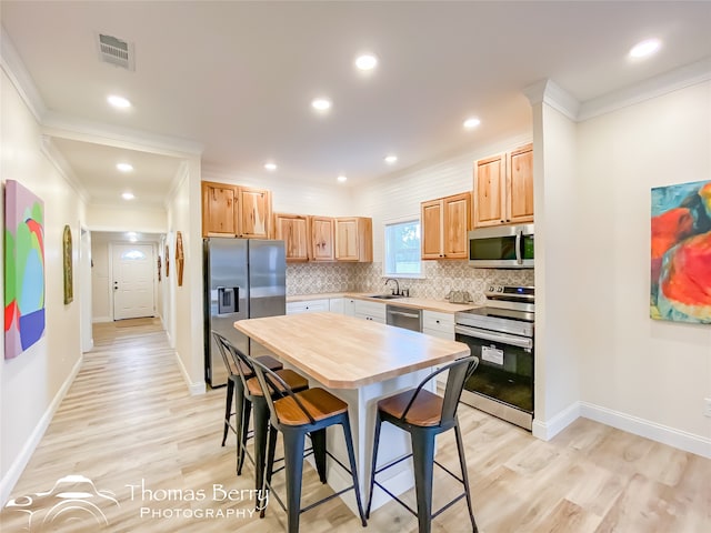 kitchen featuring tasteful backsplash, stainless steel appliances, light hardwood / wood-style floors, sink, and ornamental molding