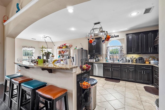 kitchen featuring appliances with stainless steel finishes, tasteful backsplash, a kitchen breakfast bar, light stone countertops, and a center island with sink