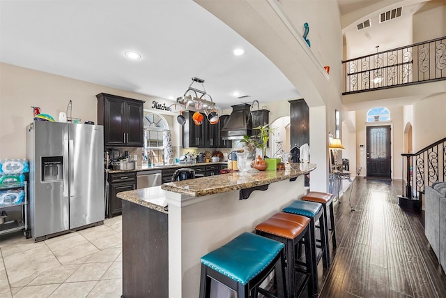 kitchen with premium range hood, appliances with stainless steel finishes, stone countertops, a breakfast bar area, and dark brown cabinetry