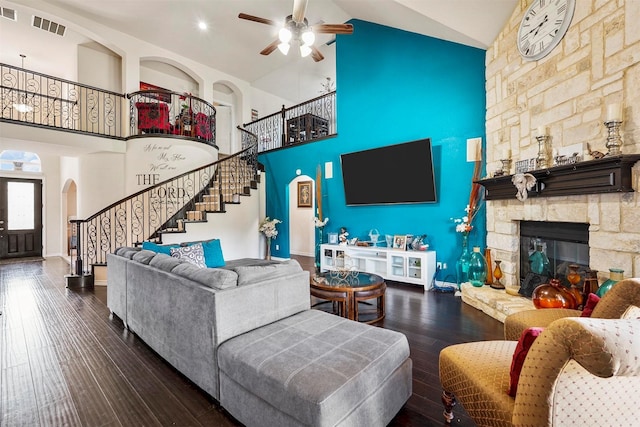 living room featuring a stone fireplace, dark wood-type flooring, high vaulted ceiling, and ceiling fan