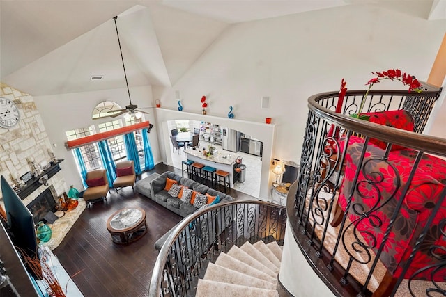 living room featuring a stone fireplace, wood-type flooring, high vaulted ceiling, and ceiling fan