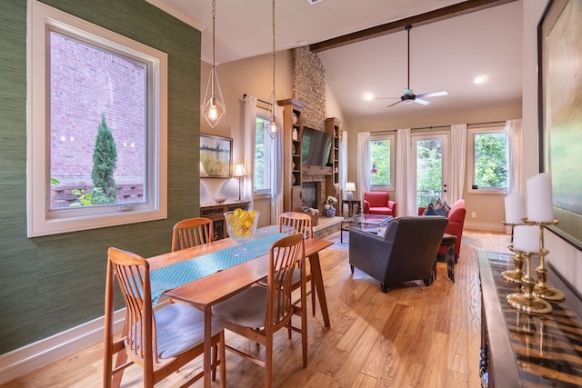 dining room featuring a stone fireplace, light wood-type flooring, ceiling fan, and high vaulted ceiling