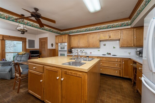 kitchen featuring ceiling fan, an island with sink, white appliances, sink, and butcher block counters