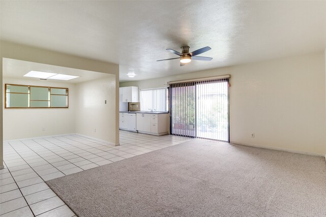 unfurnished living room with sink, ceiling fan, a skylight, and light colored carpet