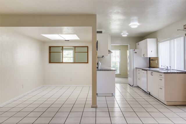 kitchen with a skylight, white cabinetry, dishwasher, and light tile patterned flooring