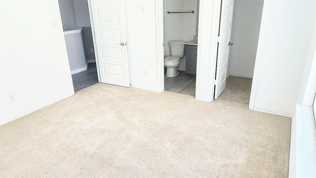 unfurnished bedroom with ensuite bathroom and light carpet