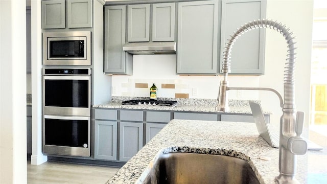 kitchen with stainless steel appliances, light stone countertops, gray cabinets, and light wood-type flooring