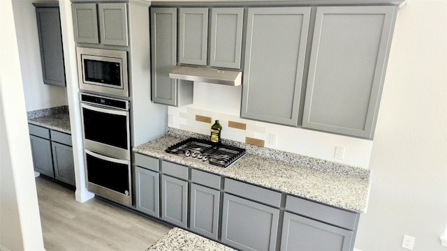 kitchen featuring gray cabinets, light stone countertops, appliances with stainless steel finishes, and light hardwood / wood-style floors