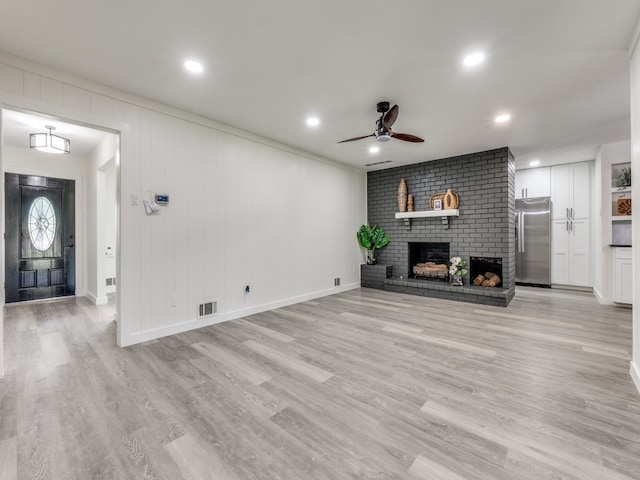 unfurnished living room with ceiling fan, a fireplace, and light hardwood / wood-style flooring