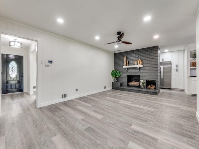 unfurnished living room with ceiling fan, a brick fireplace, visible vents, and light wood-style floors