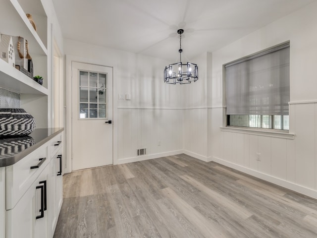 kitchen with an inviting chandelier, light wood-type flooring, white cabinets, and decorative light fixtures