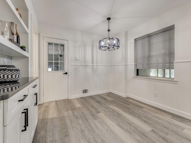 unfurnished dining area featuring light wood-type flooring, baseboards, visible vents, and a notable chandelier