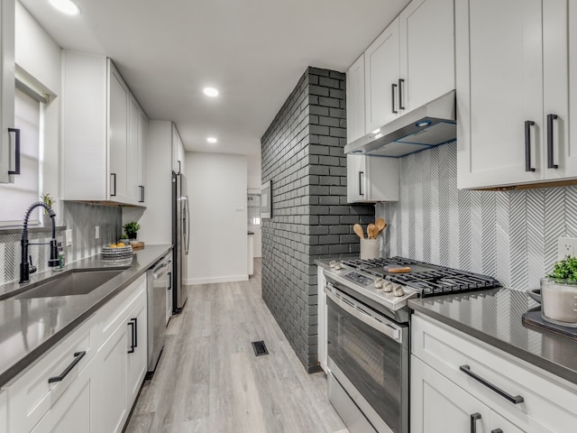 kitchen with white cabinets, stainless steel appliances, light hardwood / wood-style floors, and backsplash