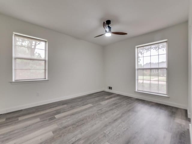 empty room featuring ceiling fan, visible vents, baseboards, and wood finished floors