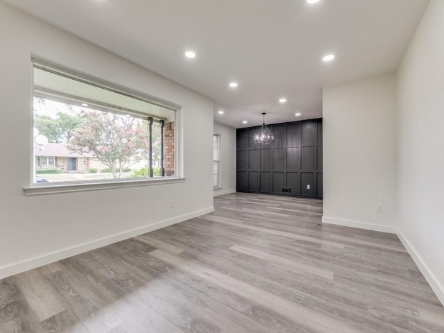 unfurnished room with light wood-type flooring, a notable chandelier, baseboards, and recessed lighting