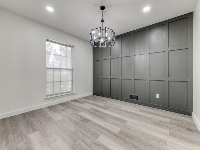 unfurnished dining area with light wood-style floors, visible vents, a decorative wall, and a notable chandelier