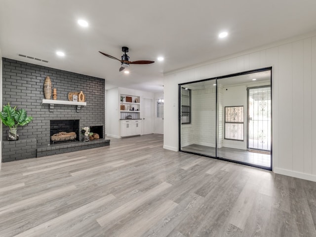 unfurnished living room featuring brick wall, a brick fireplace, ceiling fan, and light wood-type flooring