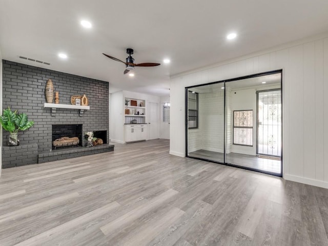 unfurnished living room with visible vents, a brick fireplace, ceiling fan, wood finished floors, and baseboards