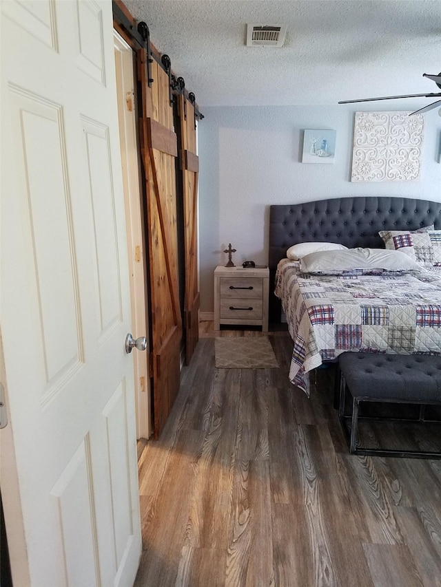 bedroom featuring wood-type flooring, a barn door, and a textured ceiling