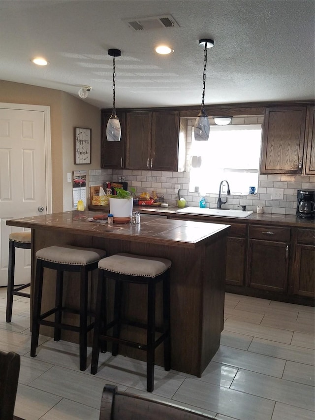 kitchen featuring dark brown cabinetry, a kitchen island, a kitchen bar, and decorative light fixtures