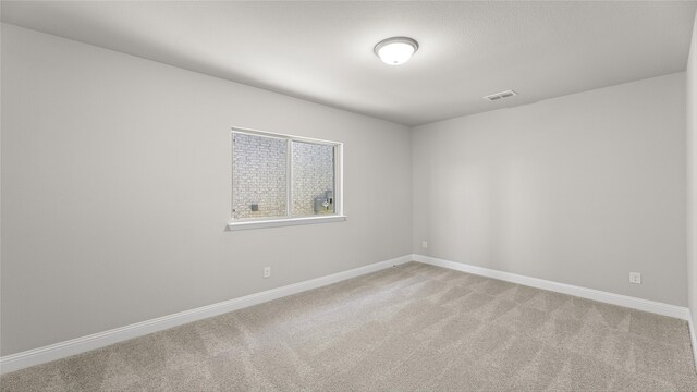 spare room featuring visible vents, light colored carpet, and baseboards