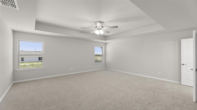 spare room featuring a tray ceiling, carpet flooring, baseboards, and a ceiling fan