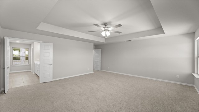 unfurnished room with visible vents, baseboards, a ceiling fan, a tray ceiling, and light carpet