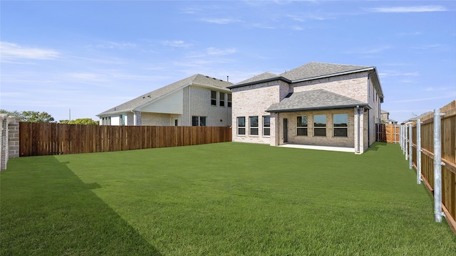 back of property featuring brick siding, a shingled roof, a fenced backyard, and a lawn