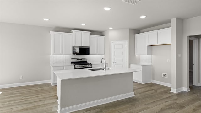 kitchen with stainless steel gas stove, black microwave, light wood-type flooring, visible vents, and a sink