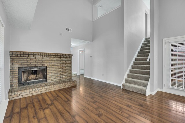 unfurnished living room featuring a textured ceiling, dark hardwood / wood-style floors, a brick fireplace, and a towering ceiling