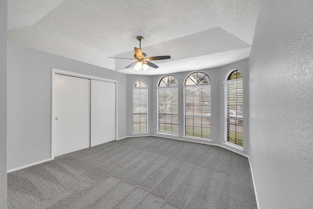 unfurnished bedroom featuring a raised ceiling, a textured ceiling, carpet floors, and ceiling fan