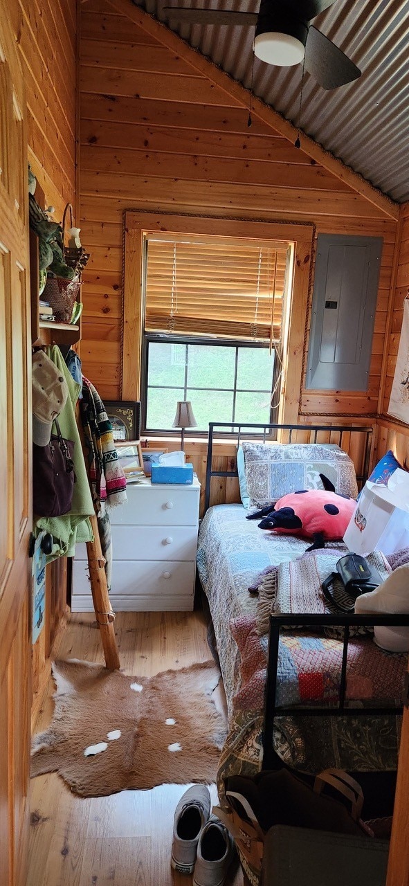 bedroom featuring wooden walls, hardwood / wood-style flooring, vaulted ceiling, and ceiling fan