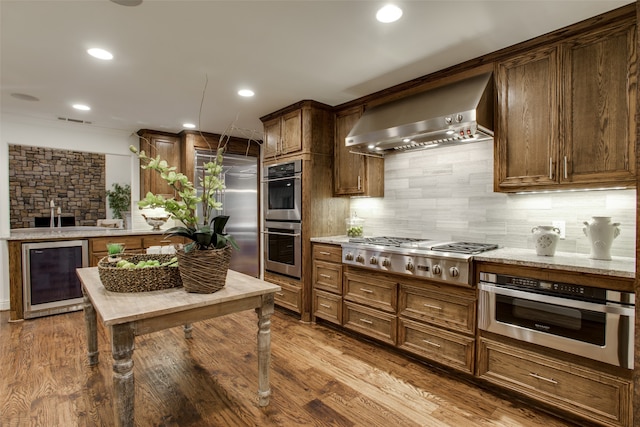 kitchen featuring wall chimney range hood, appliances with stainless steel finishes, beverage cooler, and light hardwood / wood-style floors