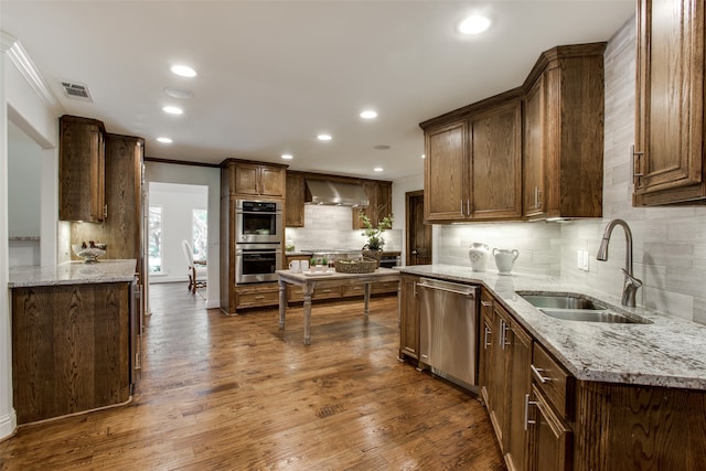 kitchen featuring tasteful backsplash, stainless steel appliances, wall chimney range hood, crown molding, and hardwood / wood-style flooring