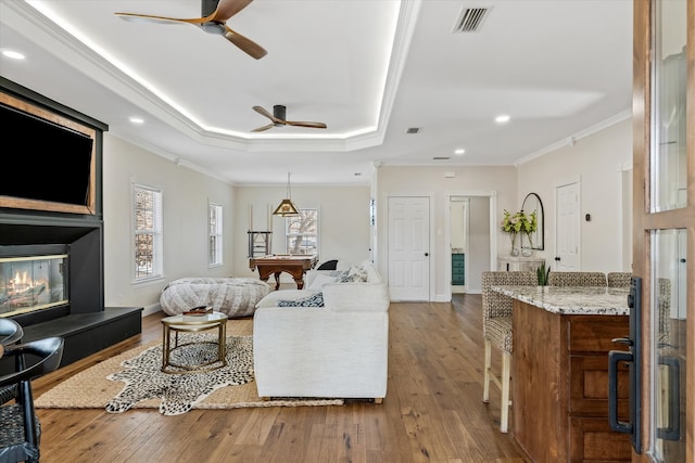 living room featuring crown molding, ceiling fan, wood-type flooring, and a raised ceiling