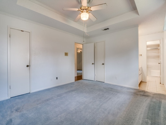 unfurnished bedroom featuring ceiling fan, a raised ceiling, crown molding, connected bathroom, and light colored carpet