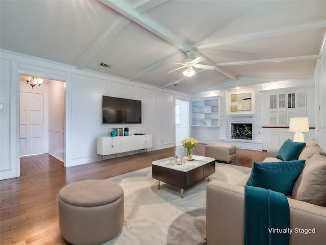 living room with lofted ceiling with beams, ceiling fan with notable chandelier, hardwood / wood-style flooring, and a large fireplace