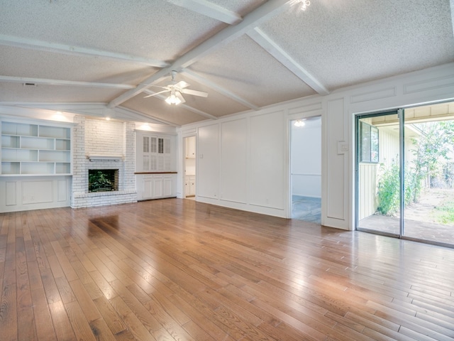 unfurnished living room featuring a textured ceiling, lofted ceiling with beams, light hardwood / wood-style flooring, ceiling fan, and a brick fireplace