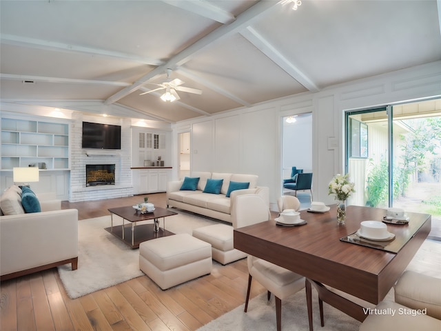 living room featuring built in shelves, lofted ceiling with beams, light wood-type flooring, ceiling fan, and a fireplace