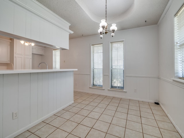 kitchen with a textured ceiling, kitchen peninsula, a notable chandelier, light tile patterned floors, and ornamental molding