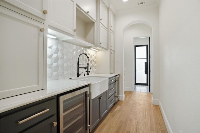 bar with decorative backsplash, beverage cooler, white cabinets, light hardwood / wood-style flooring, and sink