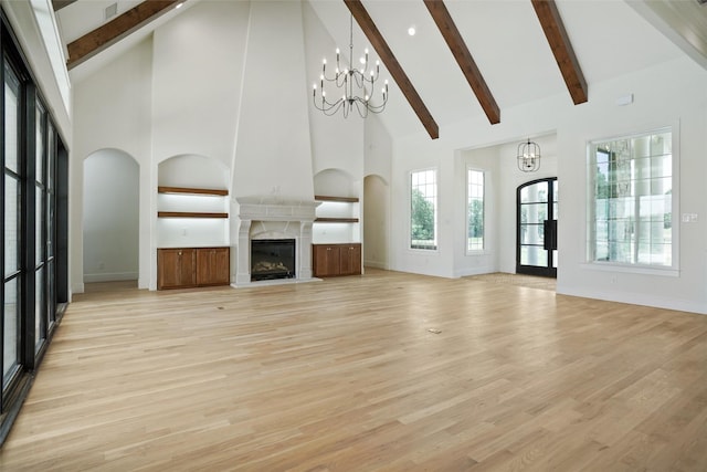 unfurnished living room featuring a high end fireplace, light wood-type flooring, a towering ceiling, and a chandelier